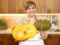 Donna sorridente mostra due tipi di zucche: una intera verde e una tagliata a metà, rivelando la polpa arancione.