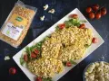 Petto di pollo impanato con **pannocchia pop corn**, servito su un letto di rucola e pomodorini. Accanto, una busta di mais per pop corn e una ciotola di pop corn.