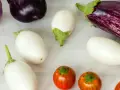 Una varietà di melanzane: lunghe e viola scuro, bianche ovali, striate viola e bianche, e piccole tonde arancioni.