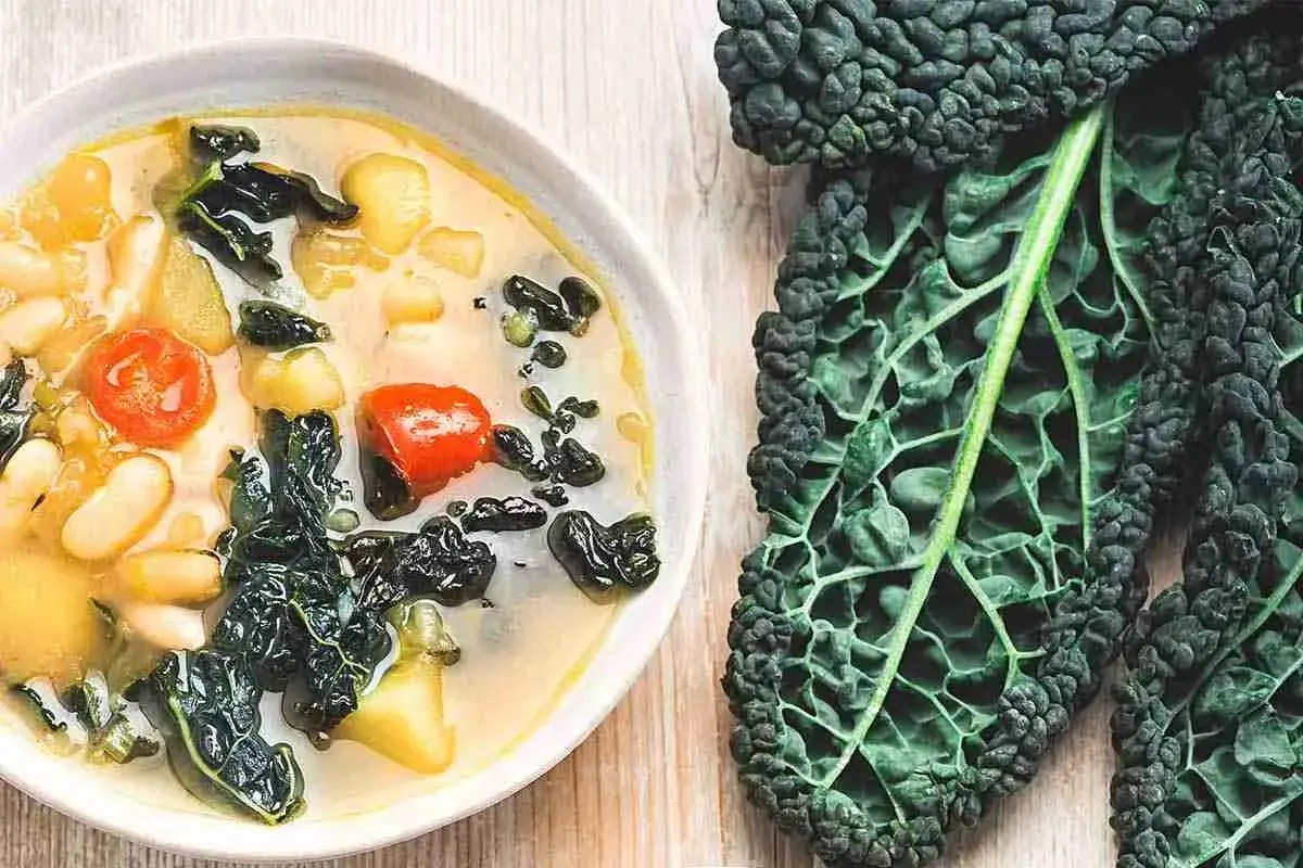 Zuppa ricca con fagioli, pomodoro e cavolo nero, accompagnata da foglie fresche di cavolo nero.