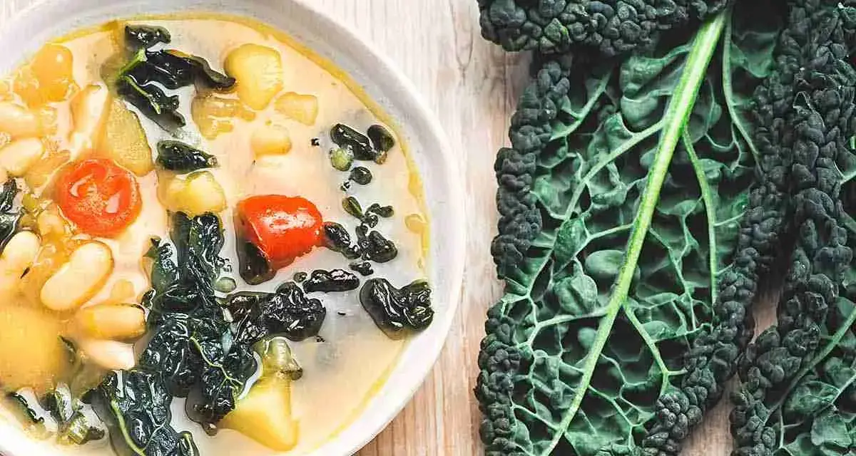 Zuppa ricca con fagioli, pomodoro e cavolo nero, accompagnata da foglie fresche di cavolo nero.