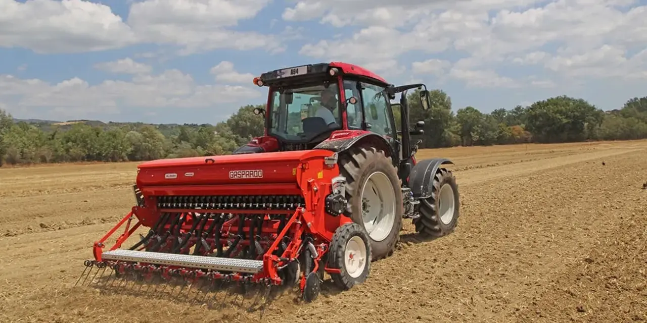 Trattore rosso con seminatrice Gasparardo in azione, un momento cruciale quando si semina il grano per il futuro raccolto.