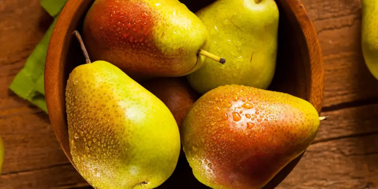 Pere succose in una ciotola di legno, pronte per essere gustate. Scopri come far maturare le pere per un sapore perfetto.