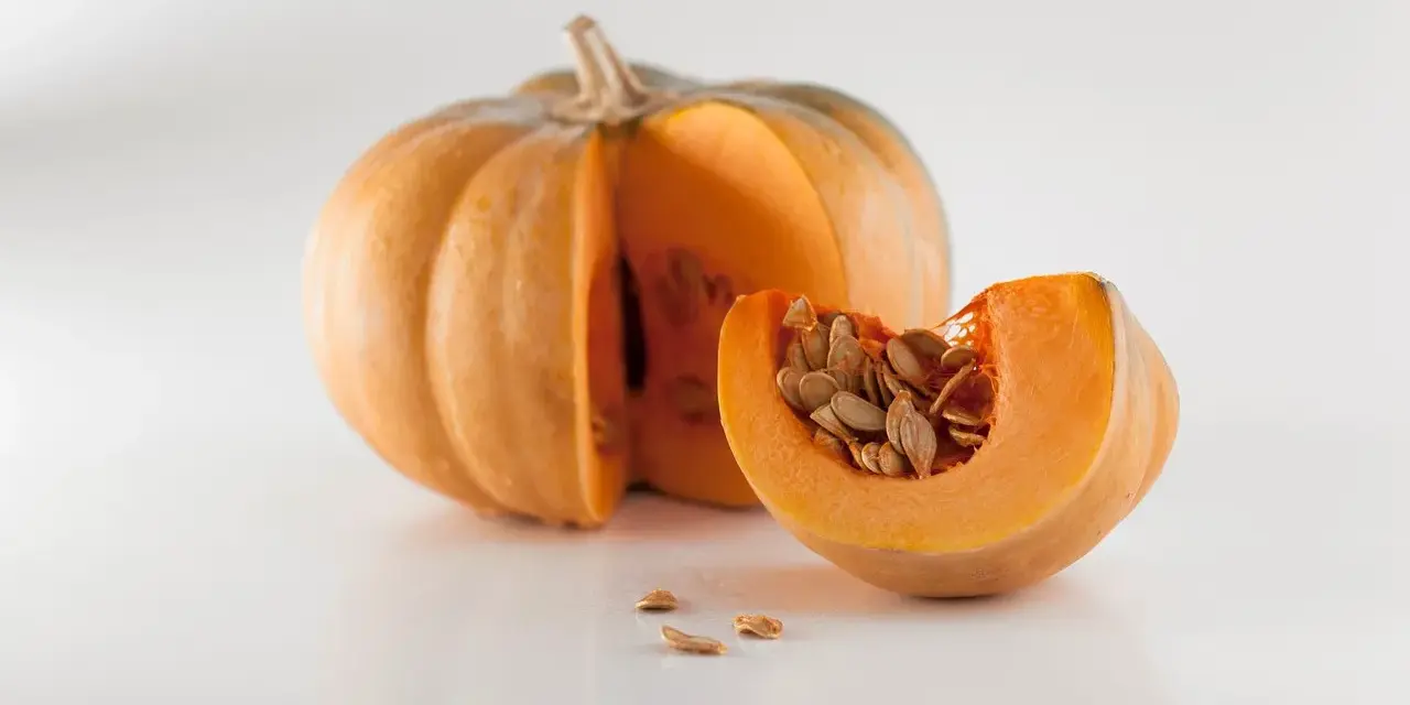 Zucca intera e una fetta con semi, un invito a pensare a quando piantare le zucche per un raccolto autunnale.