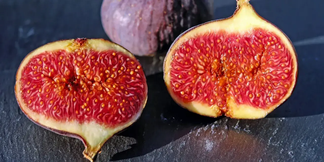 Fichi maturi, uno intero e due tagliati a metà, rivelano la loro polpa succosa. Ci si chiede dopo quanti anni fruttifica il fico per gustare queste delizie.