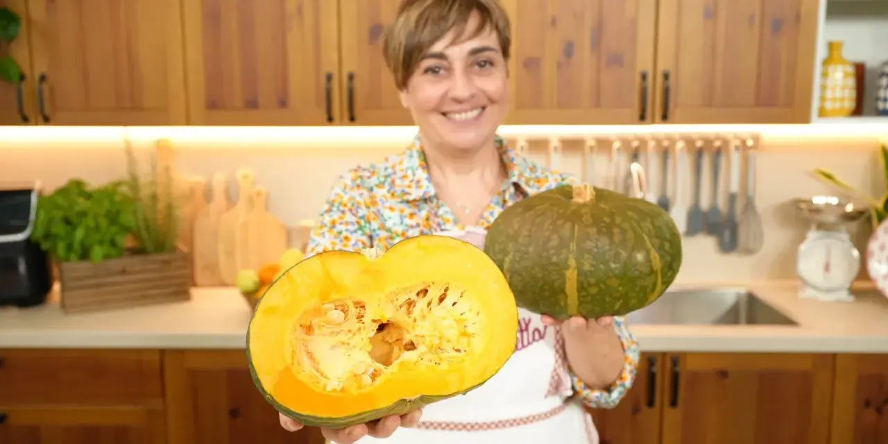 Donna sorridente mostra due tipi di zucche: una intera verde e una tagliata a metà, rivelando la polpa arancione.