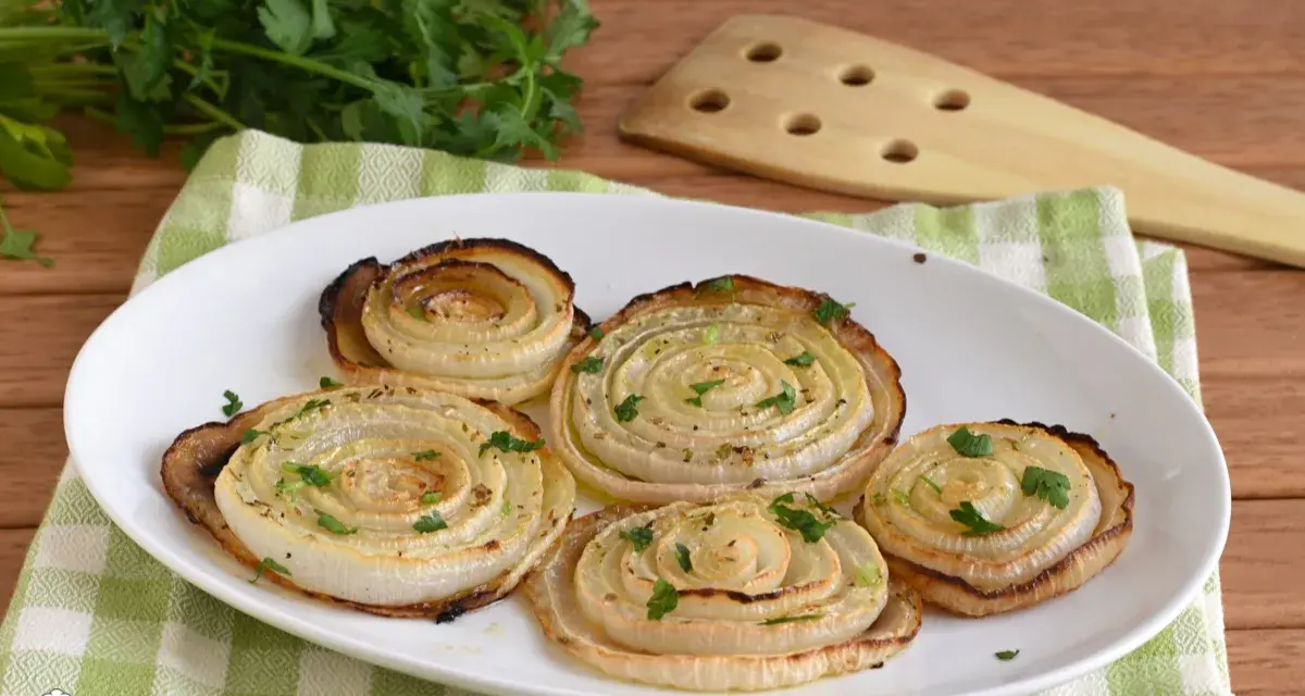 Cipolle di Giarratana al forno, cotte a spirale e guarnite con prezzemolo fresco, su un piatto bianco.