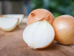 Cipolle dorate pronte per la semina. Una è tagliata a metà, rivelando la sua polpa bianca e succosa.