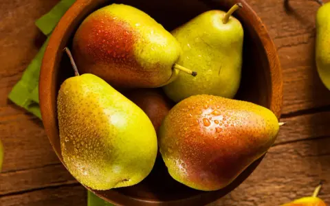 Pere succose in una ciotola di legno, pronte per essere gustate. Scopri come far maturare le pere per un sapore perfetto.