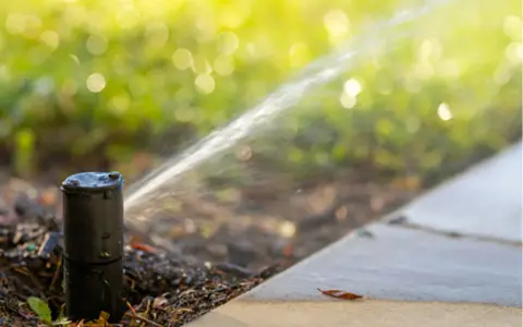 Un irrigatore automatico in azione, parte di un impianto irrigazione frutteto, spruzza acqua su un prato verdeggiante.
