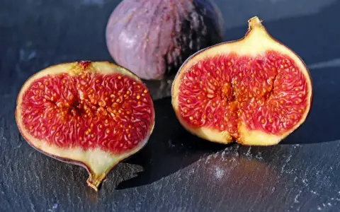 Fichi maturi, uno intero e due tagliati a metà, rivelano la loro polpa succosa. Ci si chiede dopo quanti anni fruttifica il fico per gustare queste delizie.