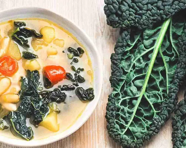 Zuppa ricca con fagioli, pomodoro e cavolo nero, accompagnata da foglie fresche di cavolo nero.