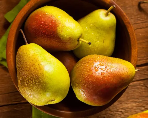 Pere succose in una ciotola di legno, pronte per essere gustate. Scopri come far maturare le pere per un sapore perfetto.