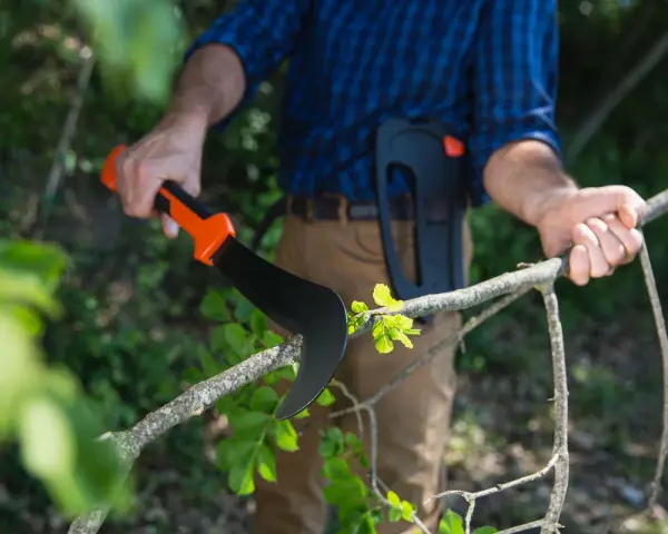 Uomo con attrezzatura per potare, impugna un falcetto affilato per tagliare un ramo verde.