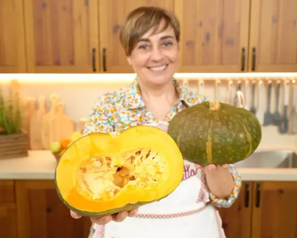 Donna sorridente mostra due tipi di zucche: una intera verde e una tagliata a metà, rivelando la polpa arancione.