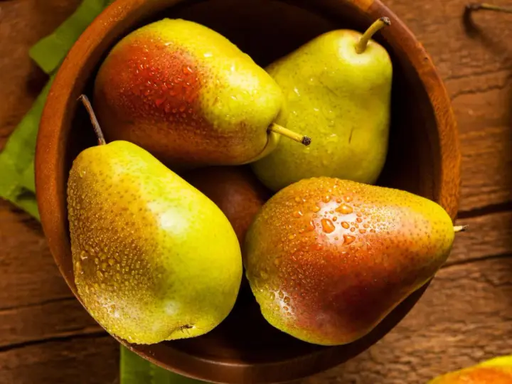 Pere succose in una ciotola di legno, pronte per essere gustate. Scopri come far maturare le pere per un sapore perfetto.