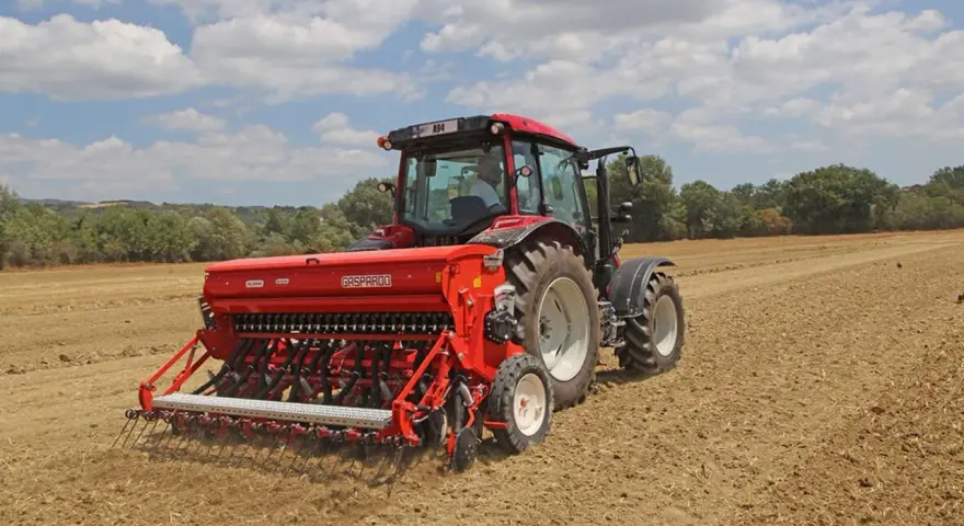 Trattore rosso con seminatrice Gasparardo in azione, un momento cruciale quando si semina il grano per il futuro raccolto.