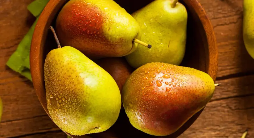 Pere succose in una ciotola di legno, pronte per essere gustate. Scopri come far maturare le pere per un sapore perfetto.