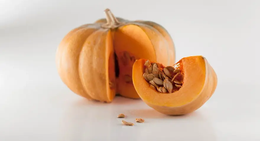 Zucca intera e una fetta con semi, un invito a pensare a quando piantare le zucche per un raccolto autunnale.