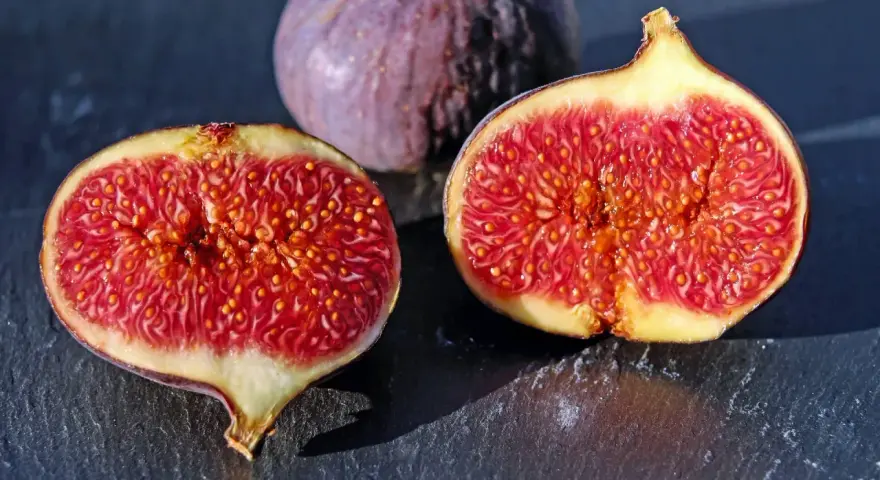 Fichi maturi, uno intero e due tagliati a metà, rivelano la loro polpa succosa. Ci si chiede dopo quanti anni fruttifica il fico per gustare queste delizie.