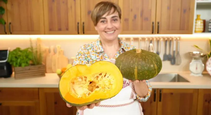 Donna sorridente mostra due tipi di zucche: una intera verde e una tagliata a metà, rivelando la polpa arancione.