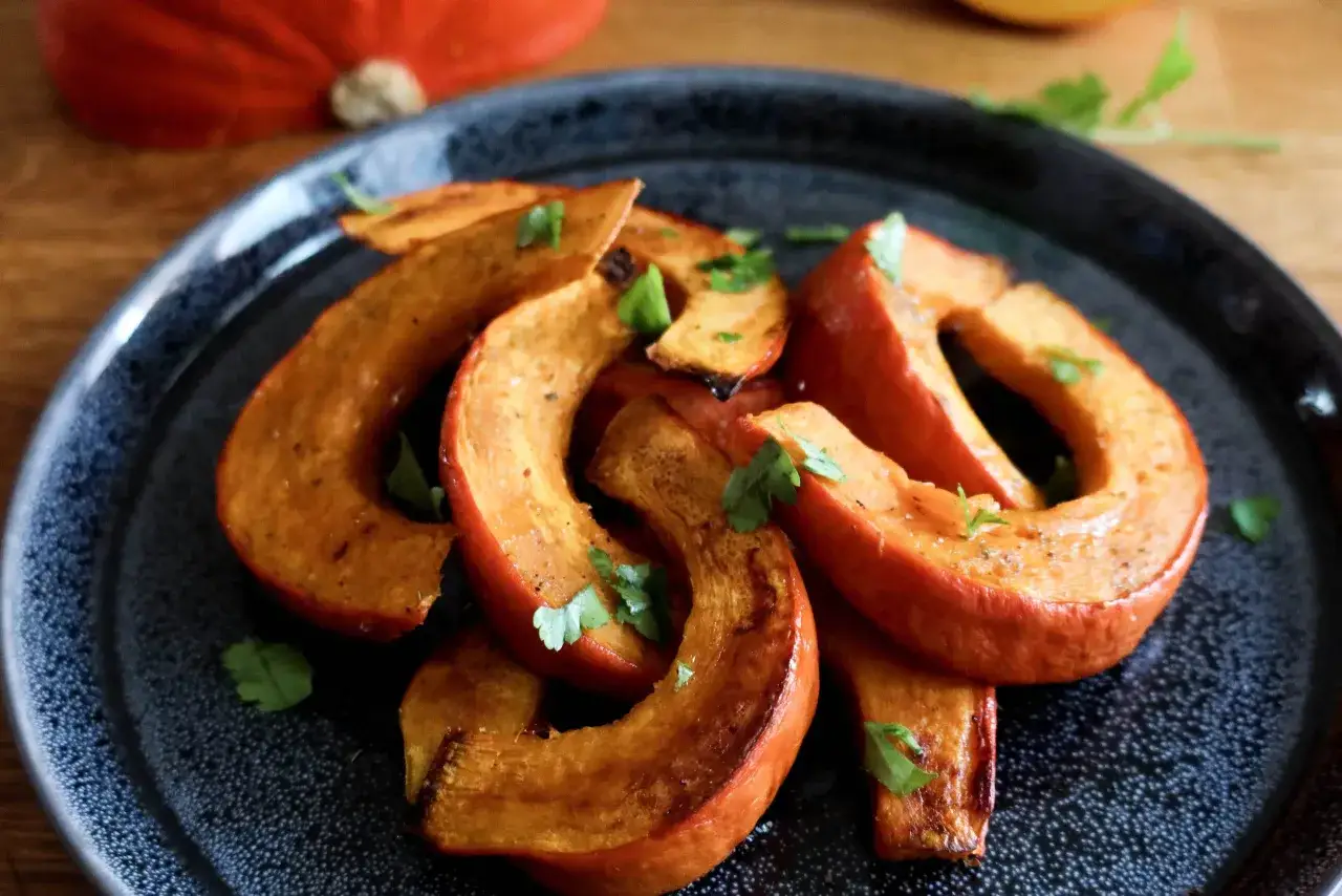 Fette arrostite di zucca Hokkaido, condite con erbe aromatiche, su un piatto scuro.