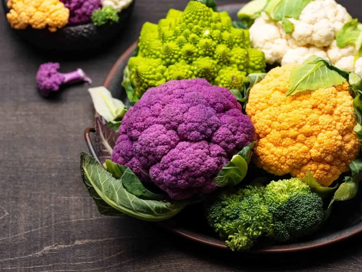 Cavolfiore viola, giallo, verde e bianco disposti su un piatto scuro. Un arcobaleno di verdure fresche.