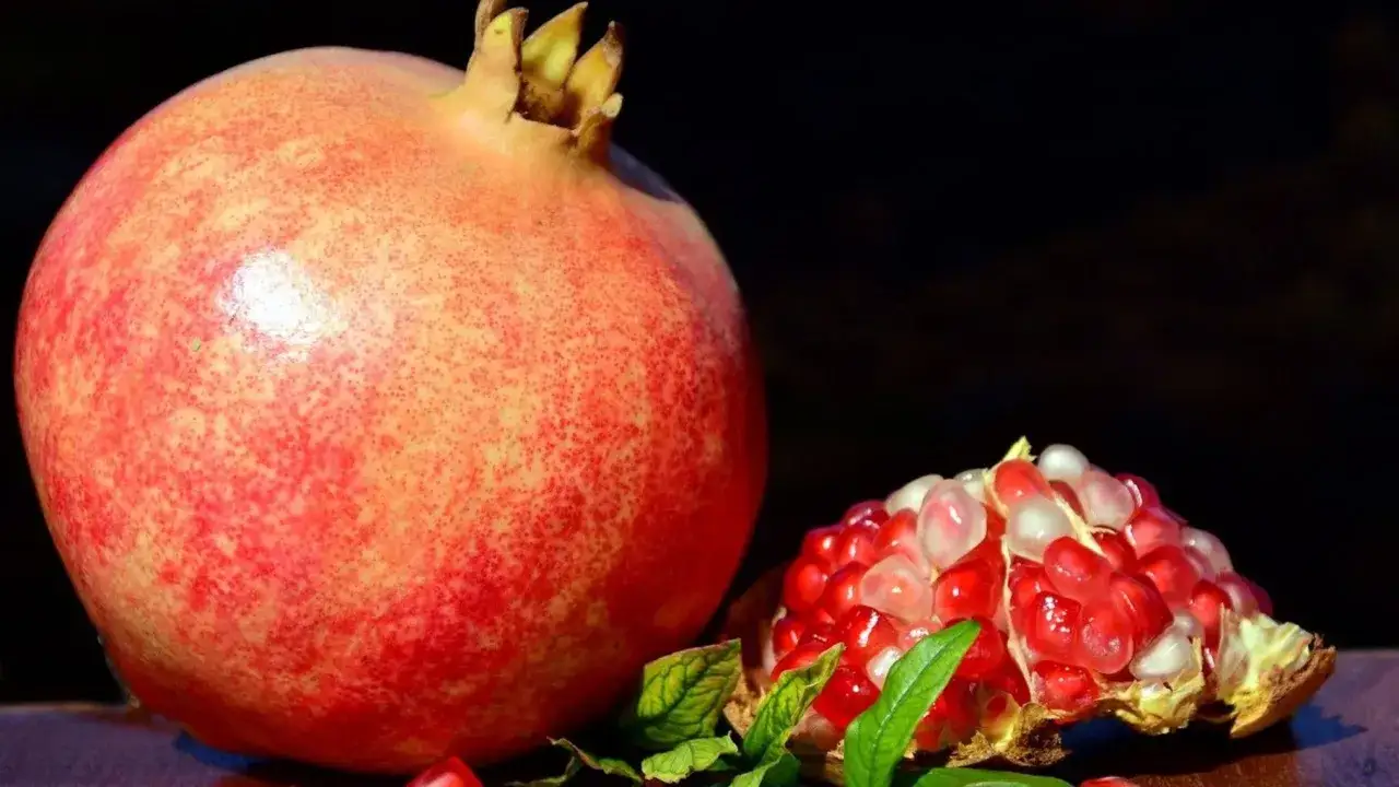 Il colore del melograno spiegazione: un frutto intero e uno aperto, rivelando i suoi chicchi rossi e traslucidi.