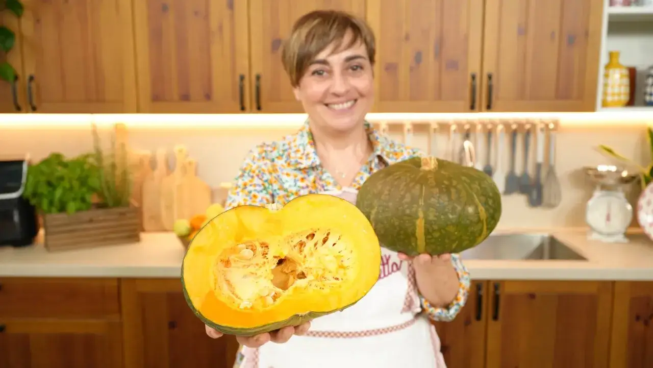 Donna sorridente mostra due tipi di zucche: una intera verde e una tagliata a met&agrave;, rivelando la polpa arancione.