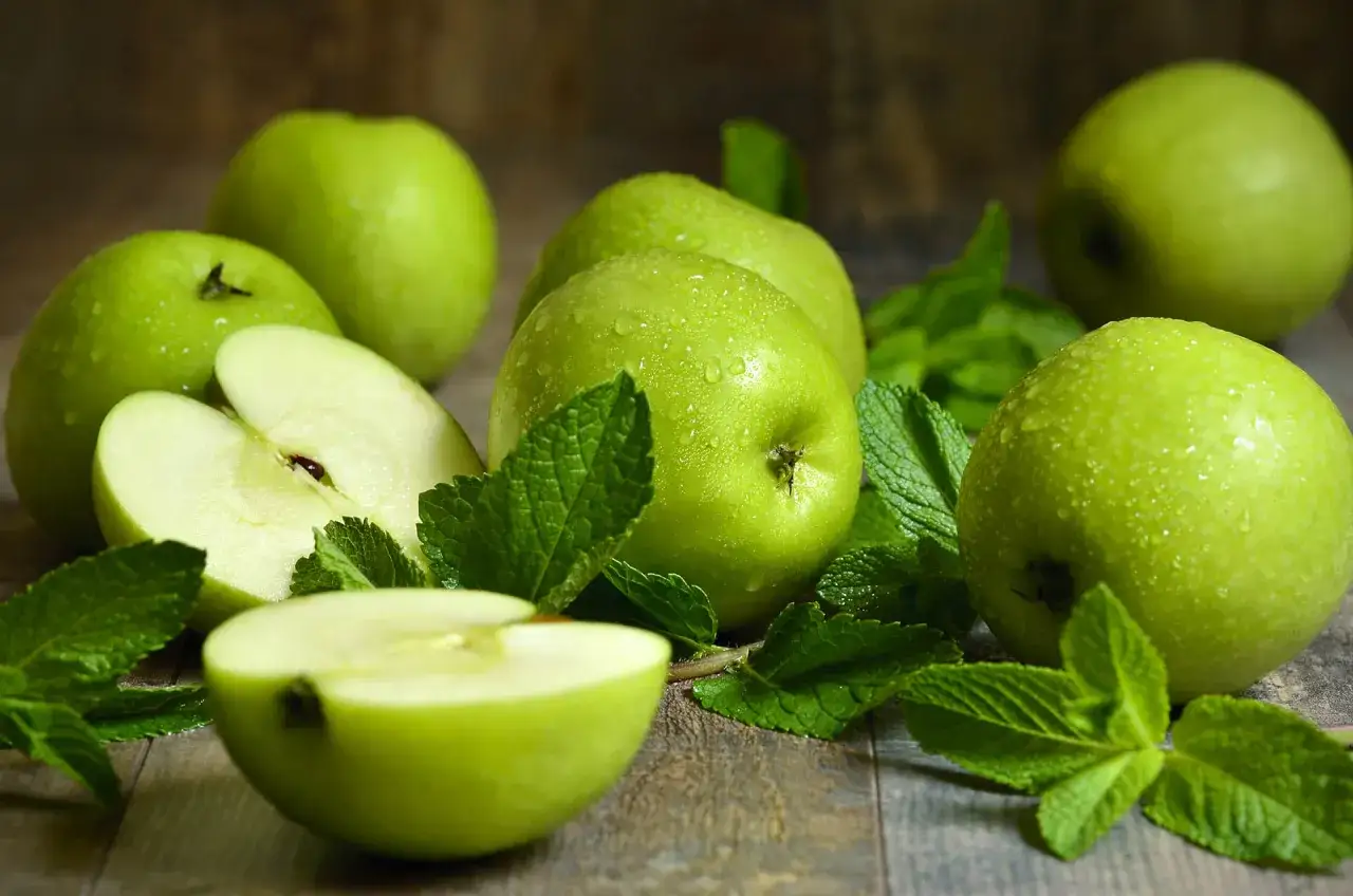 Mele verdi succose, forse Granny Smith, con gocce d'acqua e foglie di menta su un tavolo di legno.